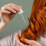 Close-up of a red-haired woman applying hair serum with a dropper.