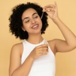 A woman with curly hair applies essential oil on her skin, promoting wellness and skincare.